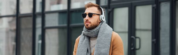 Panoramic shot of handsome man in coat and headphones outdoors - Foto, Bild