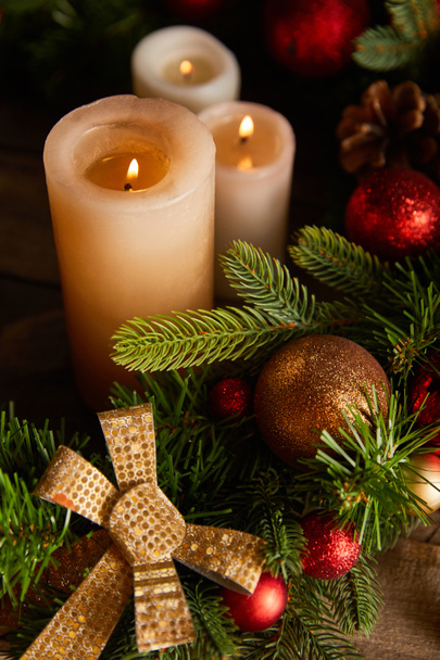 close up of burning candles with spruce branches, bow and christmas balls on wooden table - Foto, Bild