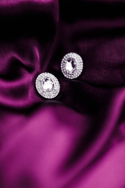 Luxusní diamantové náušnice na tmavě růžovém hedvábném tkanině, prázdninové glamou - Fotografie, Obrázek