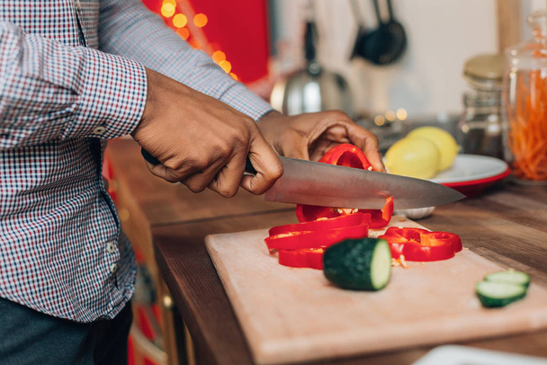African-american man cutting bell pepper in kitchen - Foto, afbeelding