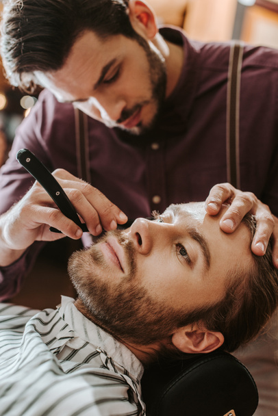 selective focus of handsome barber shaving bearded man  - Photo, Image