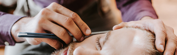 panoramic shot of barber holding razor while shaving man  - Zdjęcie, obraz