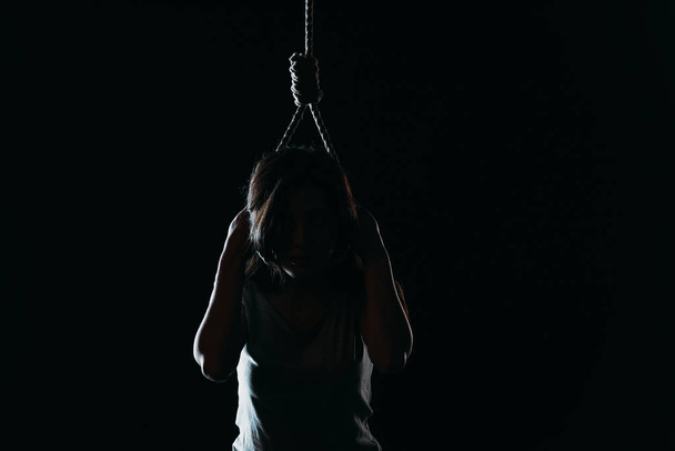 депресивна жінка, яка здійснює самогубство, одягаючи носа на шию в темряві ізольовано на чорному
 - Фото, зображення