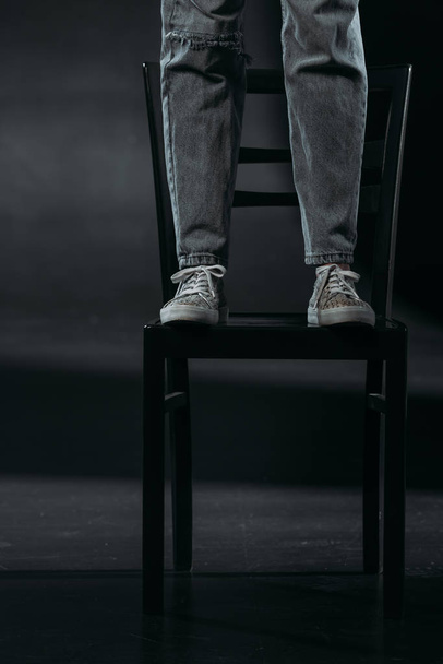 cropped view of self-destroyer standing on chair and going to commit suicide on black background - Foto, imagen