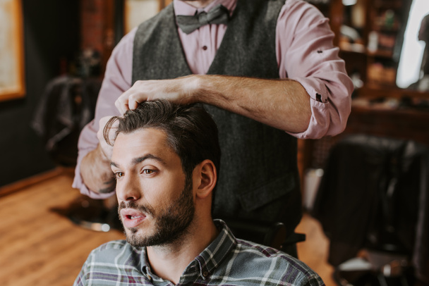 Friseur stylt Haare an gutaussehendem bärtigen Mann  - Foto, Bild