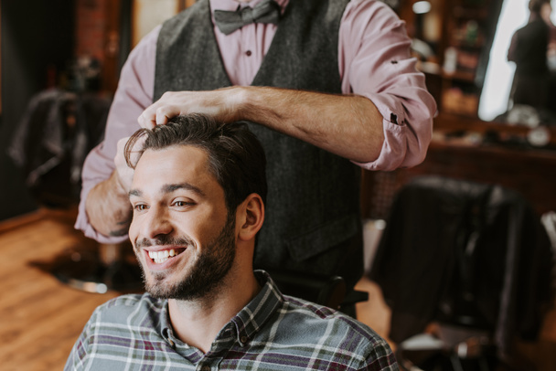 barber styling hair on cheerful bearded man  - Photo, Image