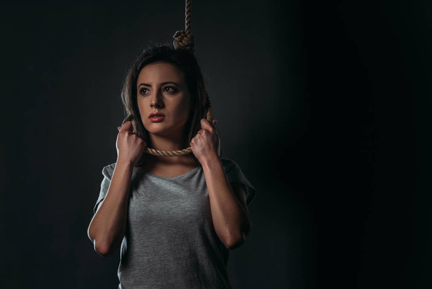 despaired woman with noose on neck looking away on black background - Foto, Imagem