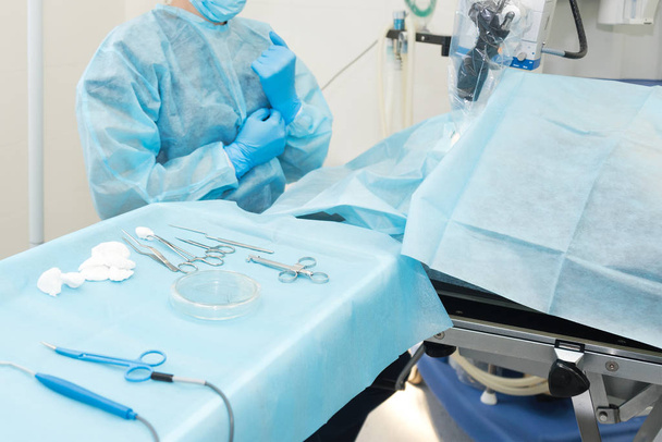 Instrumenty medyczne zbliżają się do sterylnej pieluchy. Zestaw narzędzi chirurgicznych do chirurgii plastycznej. Przyrządy i narzędzia chirurgiczne, w tym kleszcze i pęseta, umieszczone na stole - Zdjęcie, obraz