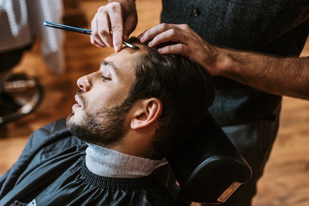 перукар тримає гостру бритву під час стрижки до красивого чоловіка
  - Фото, зображення