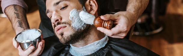 colpo panoramico di barbiere che applica la crema da barba su faccia di bell'uomo barbuto
  - Foto, immagini