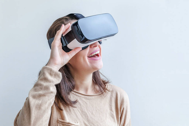 Souriez jeune femme portant en réalité virtuelle casque de lunettes VR casque sur fond blanc. Smartphone utilisant des lunettes de réalité virtuelle. Technologie, simulation, hi-tech, concept de jeu vidéo. - Photo, image