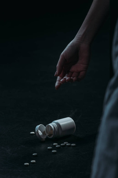 cropped view of hand of unconscious woman committed suicide by overdosing pills on dark background - Фото, зображення