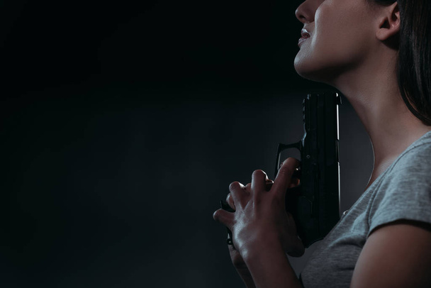 cropped view of depressed woman holding gun near chin on dark background  - Valokuva, kuva
