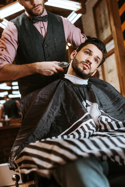 selektiver Fokus der stilvollen Friseur Halter Trimmer beim Styling Haare des Mannes  - Foto, Bild