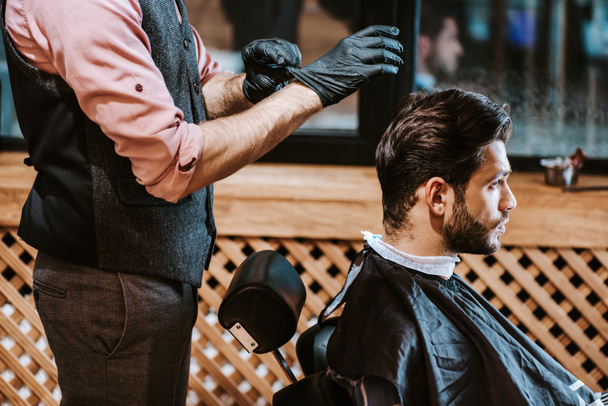 Friseur trägt schwarze Latex-Handschuhe neben Mann im Friseurladen  - Foto, Bild