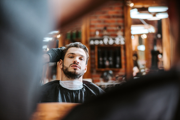 Selektiver Fokus des Friseurstyling Haare des bärtigen Mannes in der Nähe Spiegel in Friseursalon  - Foto, Bild