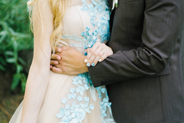 Ο γαμπρός βάζει το χέρι του γύρω από τη μέση της νύφης. Κοντινό πλάνο χεριών. Νεαρή οικογένεια και ερωτευμένο ζευγάρι - Φωτογραφία, εικόνα