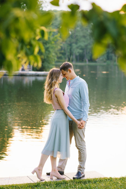 Roztomilý zamilovaný pár, zavírající oči a dotýkající se čela při procházce u jezera, když mají dovolenou. Romantický chlap domluvil rande v parku, aby si užil letní večer se svou přítelkyní - Fotografie, Obrázek