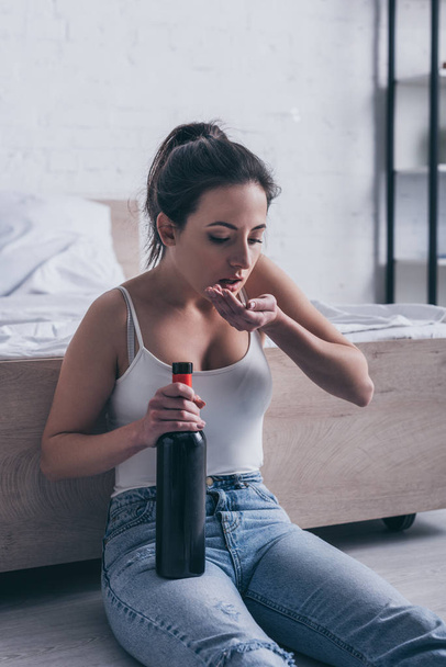 depressed young woman sitting on floor with bottle of alcohol and committing suicide by overdosing medicines - Foto, Bild