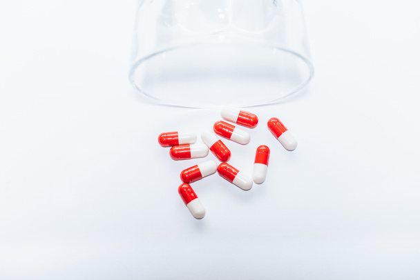 red and white capsules near overturned glass on white background, suicide prevention concept - Photo, Image
