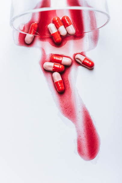omvergeworpen glas en natte pillen in rood water op witte achtergrond, zelfmoord preventie concept - Foto, afbeelding