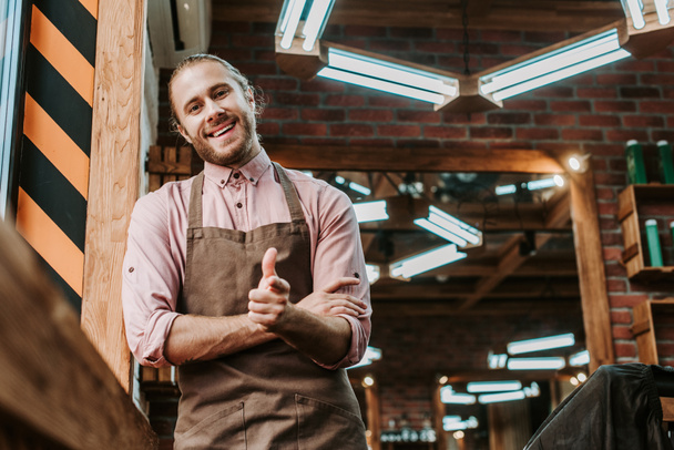 selective focus of happy barber in apron standing with clenched hands - Фото, зображення