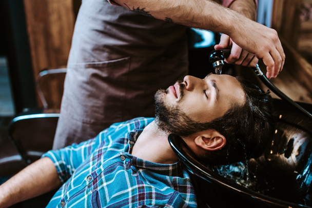 tattooed barber washing hair of bearded man with closed eyes  - Foto, immagini