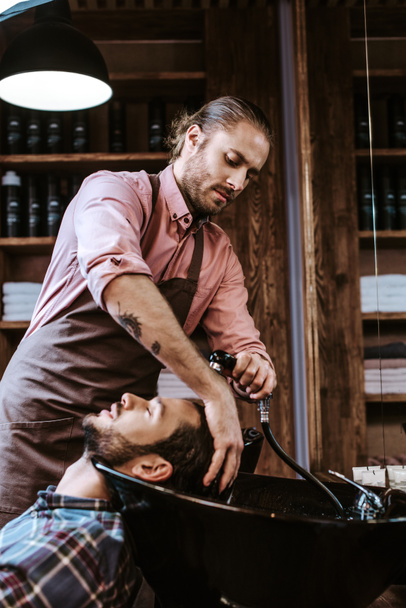 beau barbier tatoué laver les cheveux mouillés de l'homme dans un évier noir
  - Photo, image