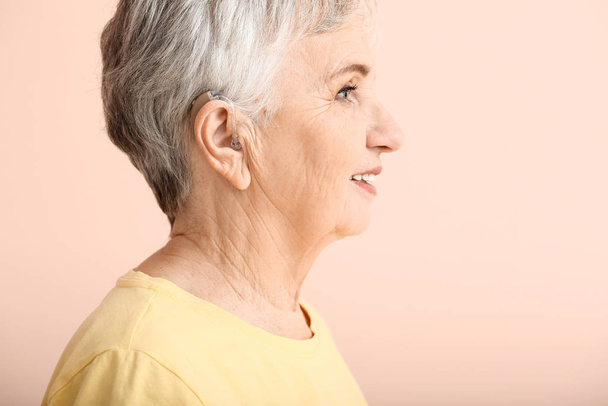 Senior woman with hearing aid on color background - Фото, зображення