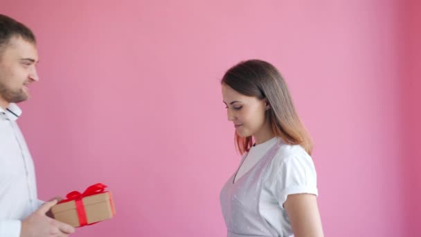 Excited girl getting gift from loving man kissing feeling happy on pink background - Imágenes, Vídeo