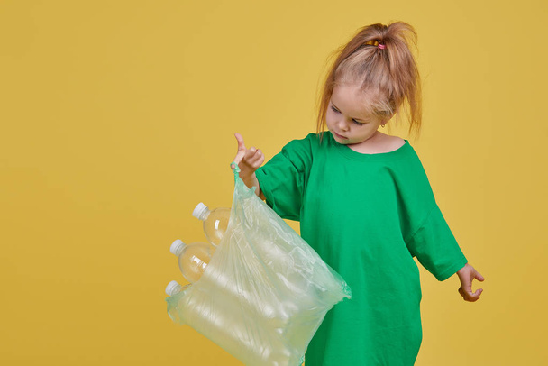 Caring for the environment. Little girl is separate plastic trash to recycle. Bright color studio background - Фото, зображення