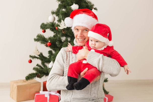 Father with his baby boy wearing Santa hats celebrating Christmas. - Zdjęcie, obraz