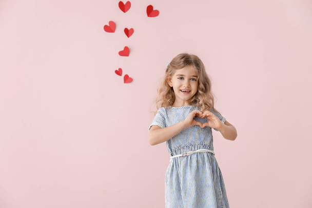 Cute little girl holding hands in shape of heart on color background. Valentines Day celebration - Photo, Image