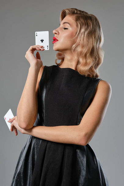 Fille blonde en robe noire élégante montrant deux cartes à jouer, posant sur fond gris. Jeux de divertissement, poker, casino. Gros plan
. - Photo, image