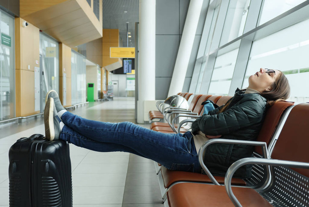 Mujer joven aburrida y cansada está esperando su vuelo en el aeropuerto sentado en el pasillo
. - Foto, imagen
