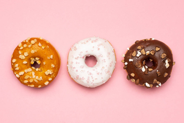 Sweet chocolate, caramel and strawberry donuts on pink background flat lay - Foto, immagini