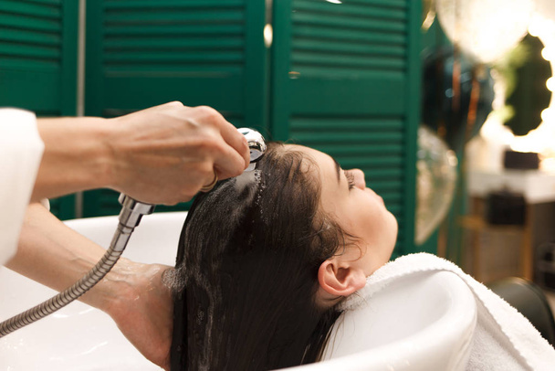 Красива молода дівчина миє голову в студії краси. Перукар миє волосся для клієнта
 - Фото, зображення