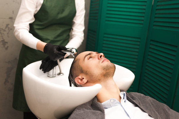 La peluquería lava los cabellos de los clientes antes de cortar. Un hombre guapo serio se lava la cabeza en un salón de belleza
 - Foto, imagen