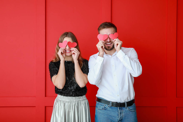 Happy young couple with red hearts on color background. Valentine's Day celebration - Photo, Image