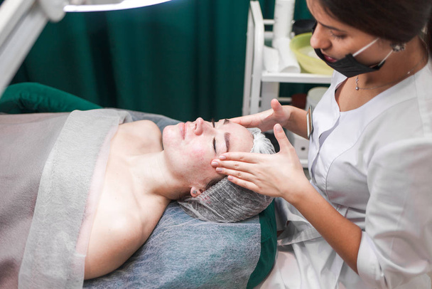 Процедура косметичного масажу обличчя вид збоку. Лікар-косметолог робить масаж на храмах
 - Фото, зображення