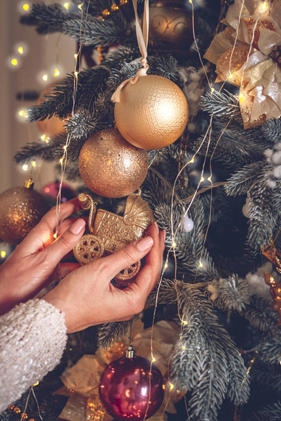 A női kezek díszítik a karácsonyfát gyönyörű üveggolyókkal. - Fotó, kép