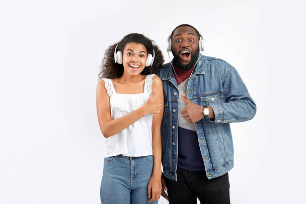Young African-American couple listening to music and showing thumb-up on white background - Foto, imagen