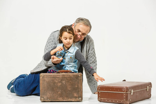 Enkelin und Großvater sitzen neben braunen alten Koffern  - Foto, Bild