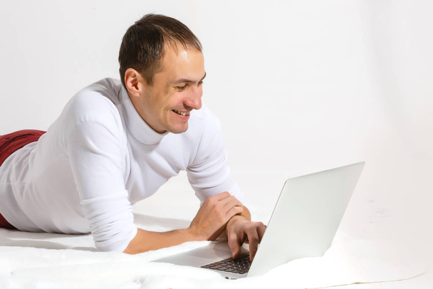 Surfing web at home. Cheerful young man lying on the floor with laptop, isolated over white background - Photo, Image