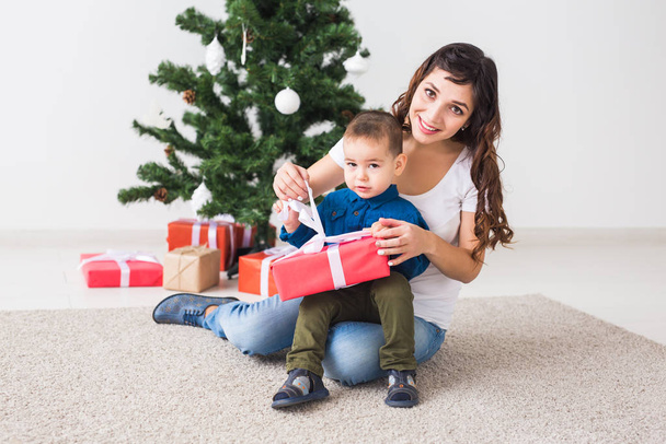 Natale, concetto di genitore single e vacanze - Carino bambino che tiene il regalo di Natale per sua madre a casa
. - Foto, immagini