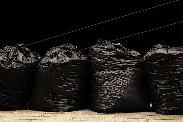 Neljä mustaa jätesäkkiä seisomassa mustaa seinää pitkin
 - Valokuva, kuva