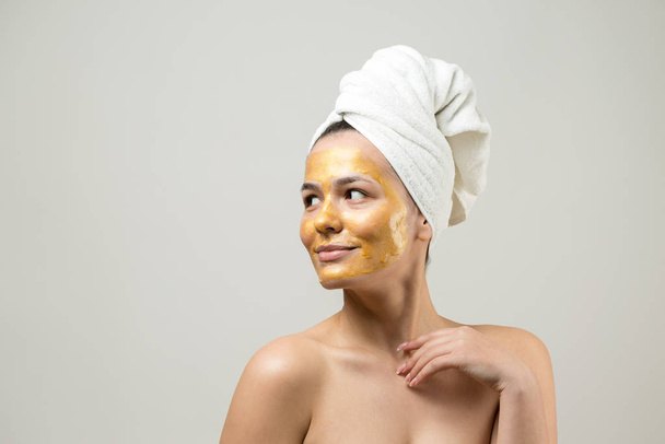 Beauty portrait of woman in white towel on head with gold nourishing mask on face. Skincare cleansing eco organic cosmetic spa relax concept. - Фото, изображение