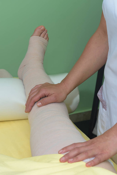 Διαχείριση λεμφαδένων: Τυλίγοντας το πόδι χρησιμοποιώντας πολυστρωματικούς επιδέσμους για τον έλεγχο του λεμφαδήμματος. Μέρος της πλήρους αποσυμφορητικής θεραπείας (cdt) και της χειρωνακτικής λεμφικής αποστράγγισης (Mld) - Φωτογραφία, εικόνα