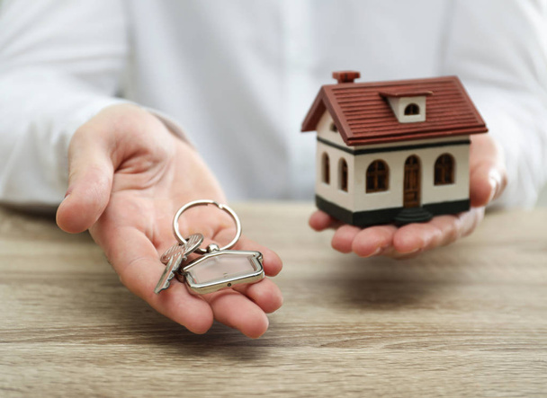 Real estate agent holding house model and key at wooden table, closeup - Foto, Bild