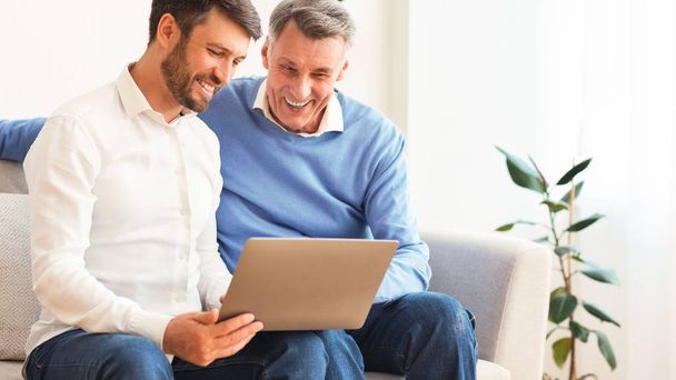 Älterer Mann erklärt älterem Vater, wie man Laptop drinnen benutzt - Foto, Bild